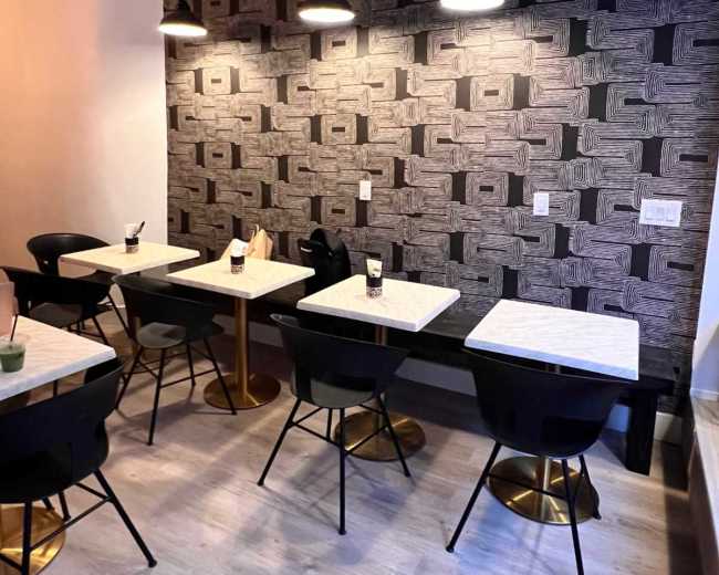 The image shows a modern café interior with several tables and chairs arranged under pendant lights against a patterned wallpaper.