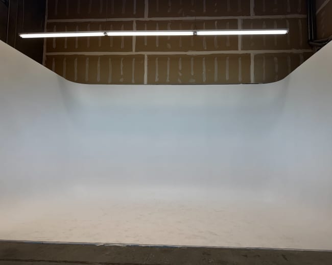 The image shows a spacious photography studio with a seamless white backdrop and exposed wooden walls.