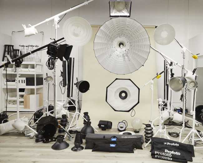 The image shows a photography studio setup featuring various lighting equipment arranged around a central backdrop.