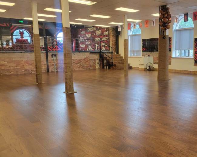 The image shows a spacious room with wooden flooring, large windows, and decorated walls featuring a red and black mural.