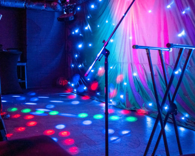 A dimly lit stage featuring colorful lights and microphone stands set up for a performance.