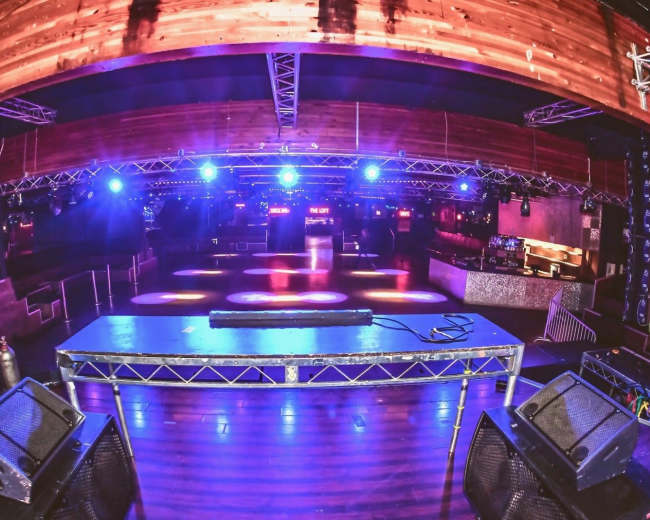 The image shows an empty nightclub interior with a DJ booth and lighting set up, illuminated by blue lights.