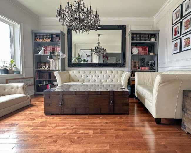 A well-furnished living room with a chandelier, a large mirror, two sofas, a wooden coffee table, and a bookshelf against the wall.