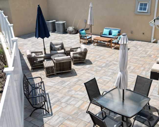 The image shows a spacious outdoor patio area with various seating arrangements, including a table with chairs, lounge furniture, and umbrellas.