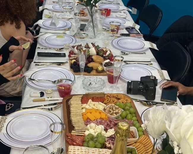A long dinner table elegantly set with white plates, a variety of food platters, and decorative flowers, ready for a gathering.