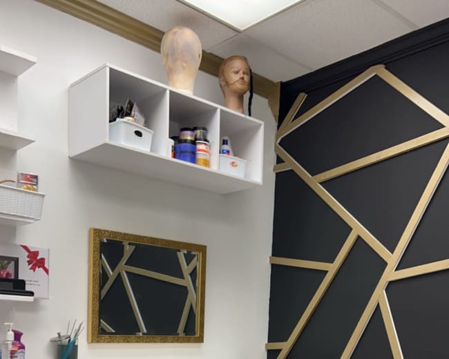 The image shows a corner of a salon with a chair, a mirror in a gold frame, and shelves containing various hair and beauty products.