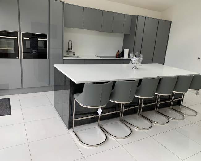 The image shows a modern kitchen with gray cabinetry, a white countertop, and six bar stools arranged at a large island.