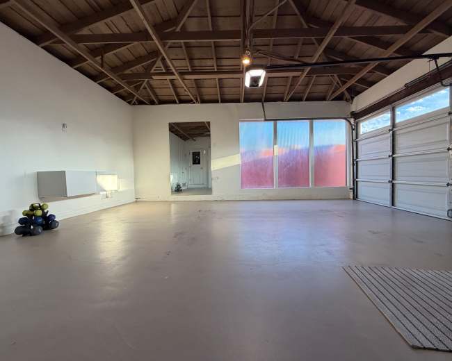 The image shows an empty garage with a wooden ceiling, a large window, and a few exercise weights in the corner.