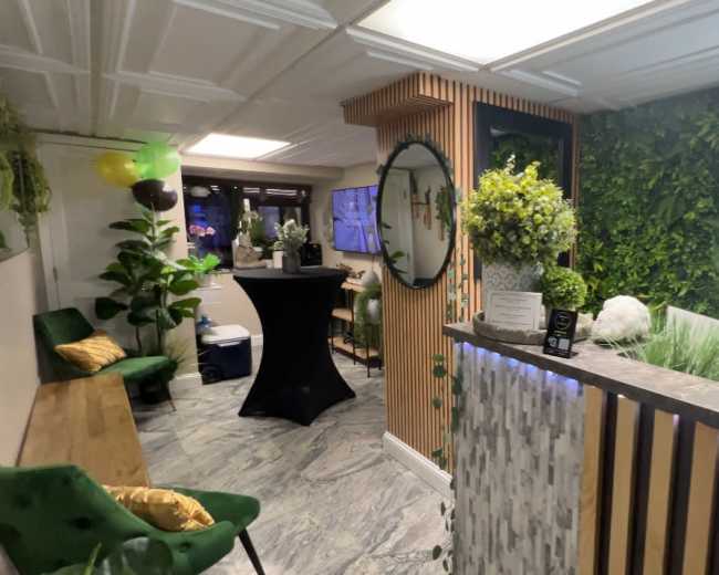 The image shows a modern beauty salon reception area with green plants, a stylish counter, and seating arrangements.