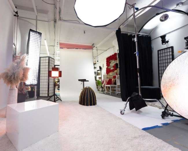 The image shows a photography studio setup with various light sources, backdrops, and props arranged on a carpeted floor.