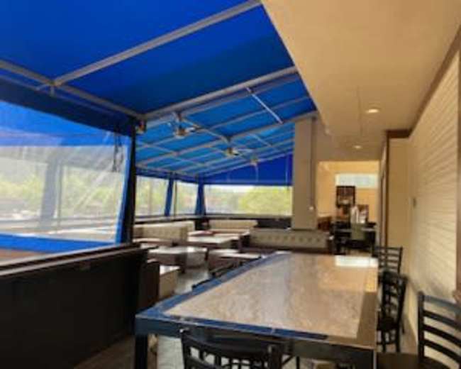 A restaurant patio with blue canopies, a large table, and empty seating areas.