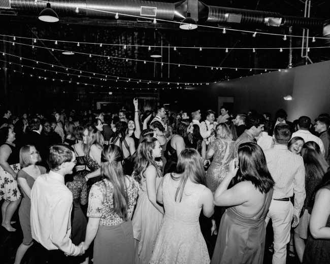 A lively crowd of people dances in a dimly lit venue adorned with string lights.