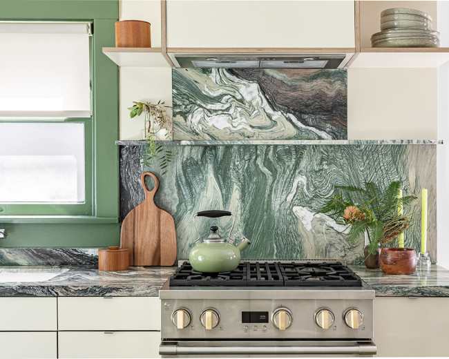 A modern kitchen with a green and marble-patterned backsplash, a stainless steel stove, and wooden accents.