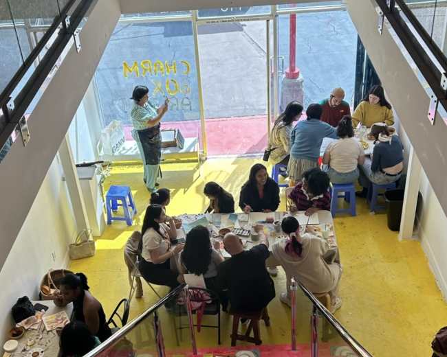 A busy café scene with customers seated at tables on the ground floor, viewed from a staircase.