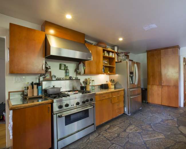 The kitchen features wooden cabinets, stainless steel appliances, and a stone floor, with a layout that includes a gas stove and a large refrigerator.