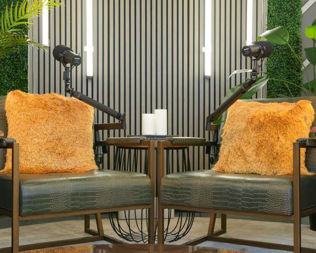 Two chairs with orange fluffy pillows are positioned opposite each other, surrounded by greenery and accent lighting.