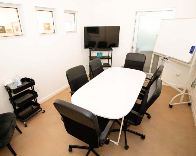 A small conference room with a white table, six black chairs, a television, and a whiteboard.