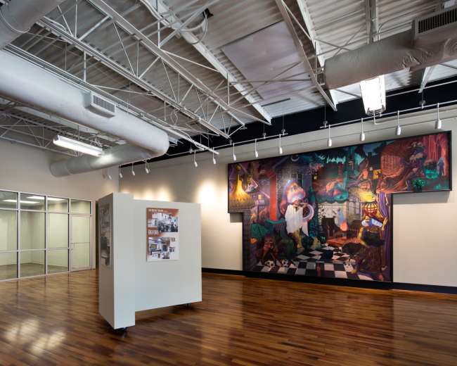 The interior of a modern commercial space features polished wood flooring, exposed ductwork, and a large mural on the wall alongside a central display structure.