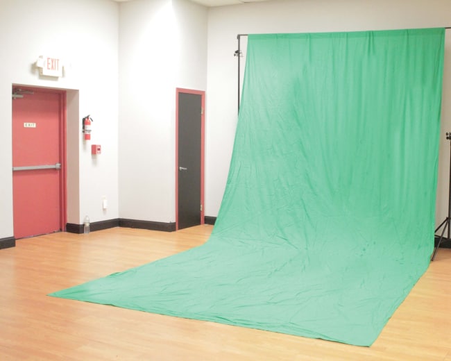 A green backdrop set up in a room with wooden flooring and plain walls.