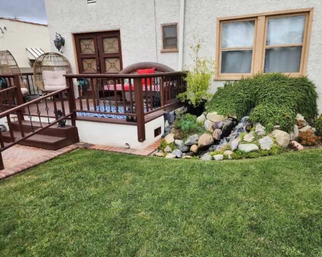 A landscaped backyard with a garden area featuring rocks, a small water feature, and a wooden deck with seating.