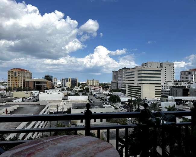 The image shows a city skyline with various buildings and a clear blue sky dotted with clouds.