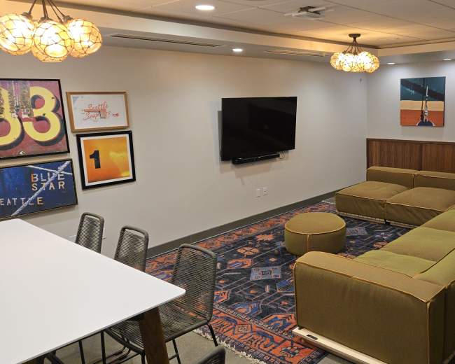 The image shows a modern lounge area with a large green sectional sofa, a television mounted on the wall, and a decorative rug on the floor.