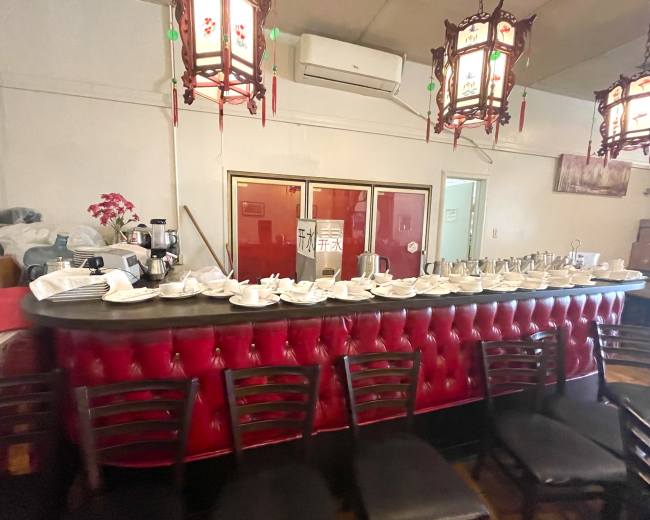 The image shows a red velvet bar with various teapots and dishes arranged on top, set against a backdrop of wall décor and hanging lanterns.