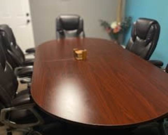 A large oval conference table surrounded by ergonomic black chairs is set in a room with a blue wall and decorative elements.
