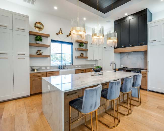The image shows a modern kitchen with a marble island, brass-accented bar stools, and cabinets in a mix of light and dark wood finishes.