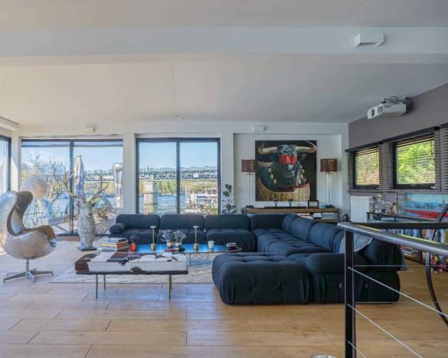 The spacious living room features large windows overlooking a water view, a sectional sofa, and modern decor elements.