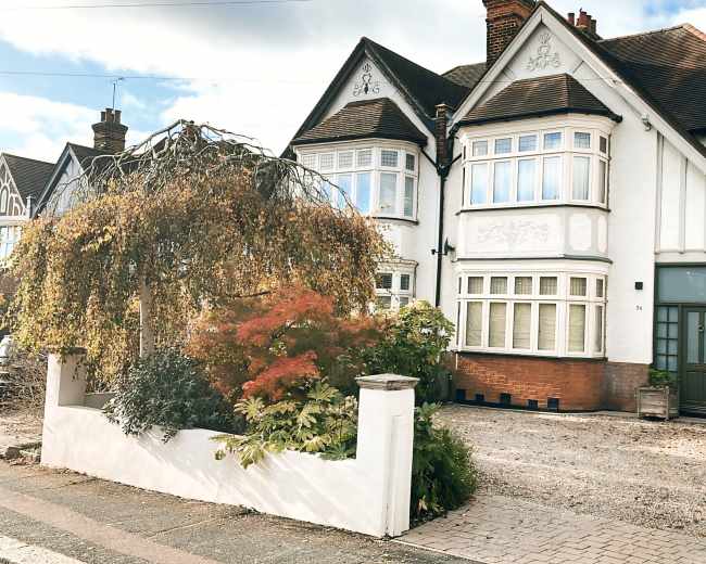 A large, two-story house with a pointed roof and a manicured front garden is located on a gravel driveway.