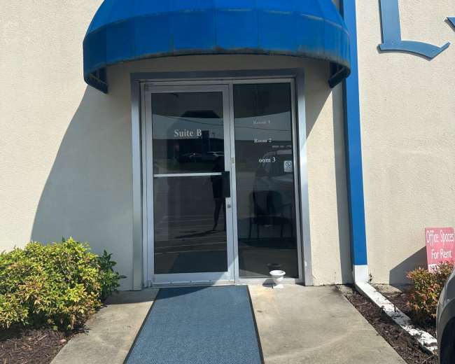 The entrance of a commercial building features a blue awning above double glass doors, with a blue mat leading to the entrance.