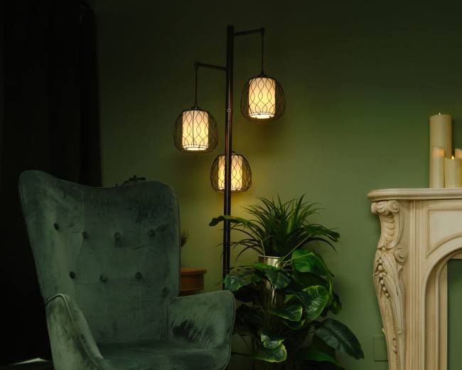 The image features a green velvet chair beside a decorative floor lamp and a potted plant, set against a muted green wall.