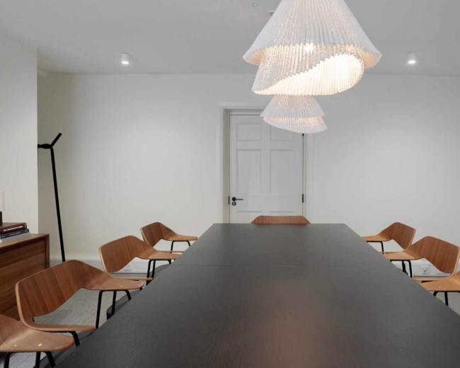 The image shows a modern conference room with a long black table surrounded by wooden chairs and illuminated by decorative pendant lights.