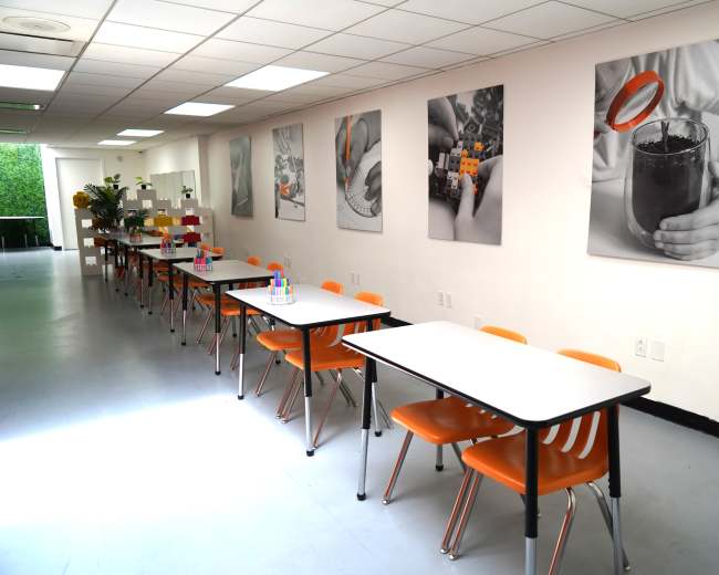 A long room features multiple tables with orange chairs, adorned with black and white photographs on the walls.