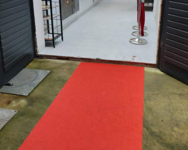 The image shows a red carpet leading into an art gallery with multiple paintings displayed on the walls.