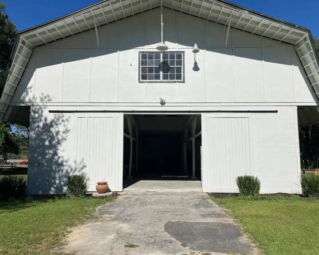 A white barn with open sliding doors and a large window at the center of the gable.
