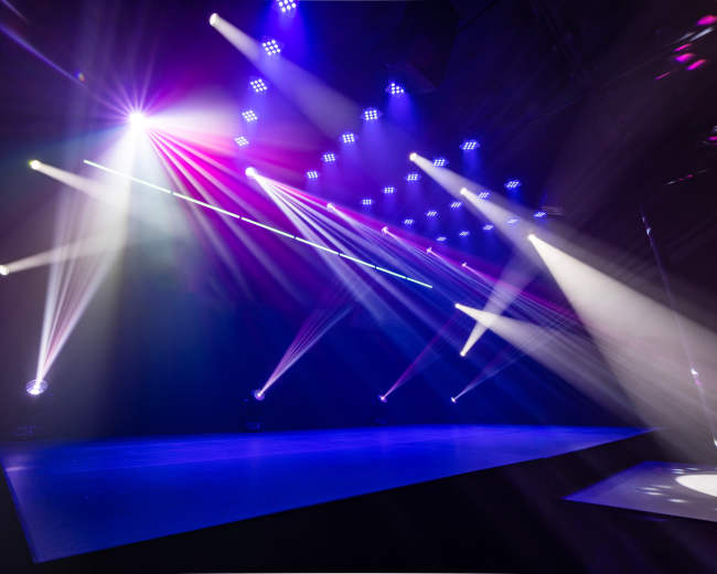 Colorful stage lights illuminate an empty performance area with beams of light projecting in various directions.