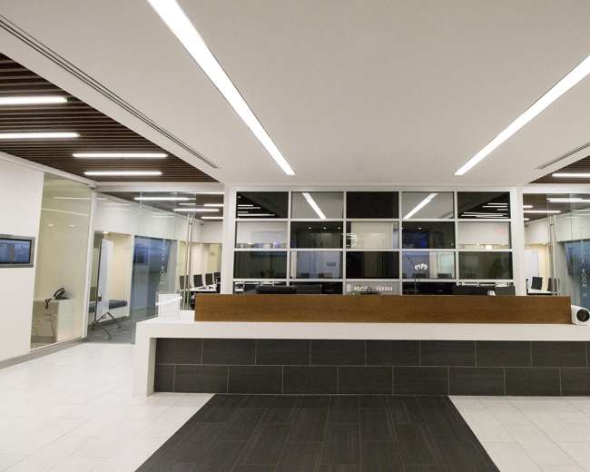 A modern reception area with a central wooden desk and glass partitions, featuring a minimalist design and fluorescent lighting.