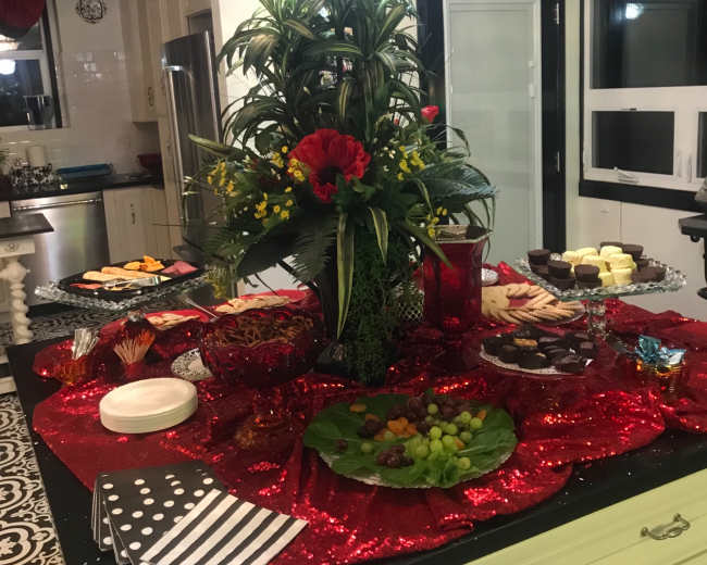 A decorative kitchen island adorned with a large floral centerpiece and various dishes of appetizers and desserts arranged on a red sparkly tablecloth.