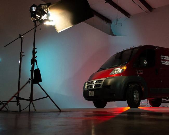A red delivery van is positioned in a studio setting with professional lighting equipment surrounding it.