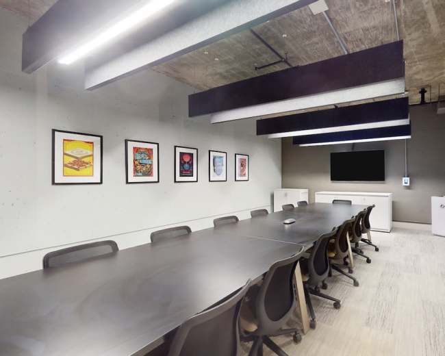 A modern conference room features a large table surrounded by chairs, adorned with framed artwork on the walls and equipped with a TV and whiteboard.