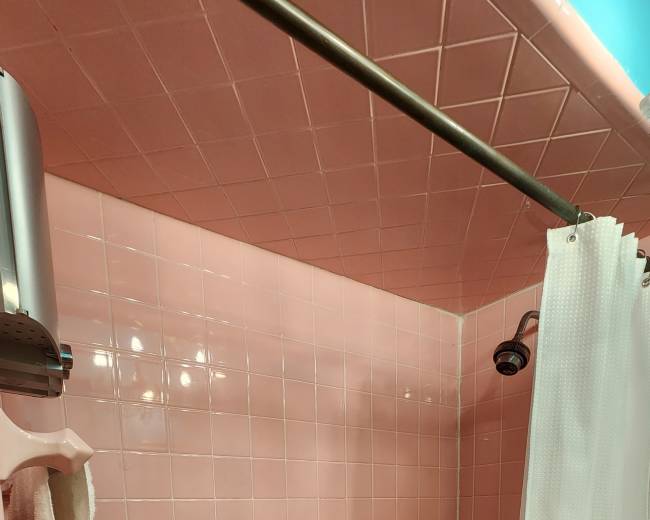 The image shows a pink tiled bathroom with a bathtub and a shower curtain.