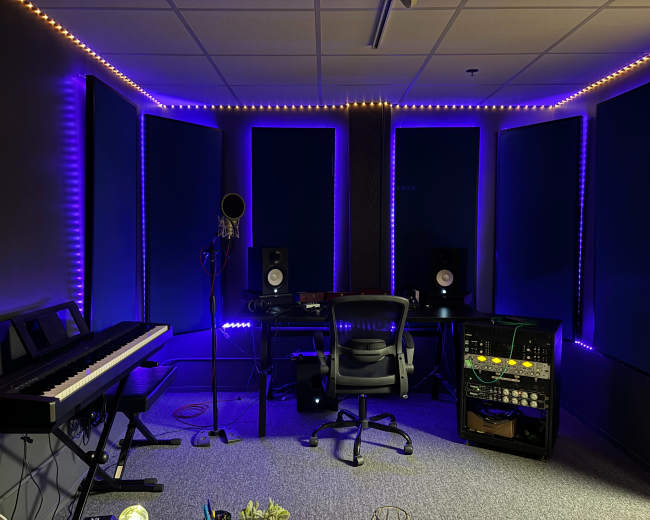 The image shows a music studio with a keyboard, microphone, monitors, and ambient lighting along the walls.