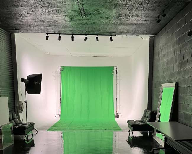 A photography studio with a green backdrop, equipped with lights, chairs, and reflective surfaces on the floor.