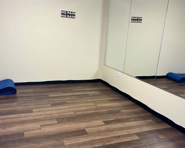 A fitness room with wooden flooring, two yoga mats rolled up against the wall, and motivational signs on the walls.