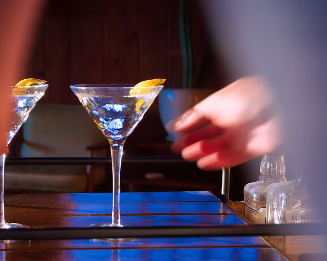 A hand reaches to pick up a martini glass on a table with another glass nearby.