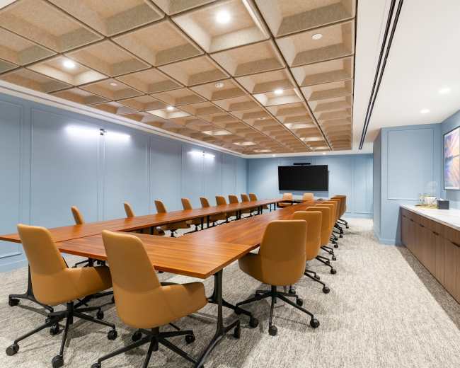 The image shows a modern conference room with a large table, multiple ergonomic chairs, and acoustic ceiling tiles.