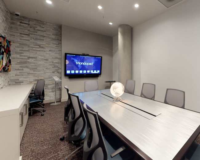 The image shows a modern conference room with a long table, several chairs, a television screen on the wall, and a decorative globe in the center.