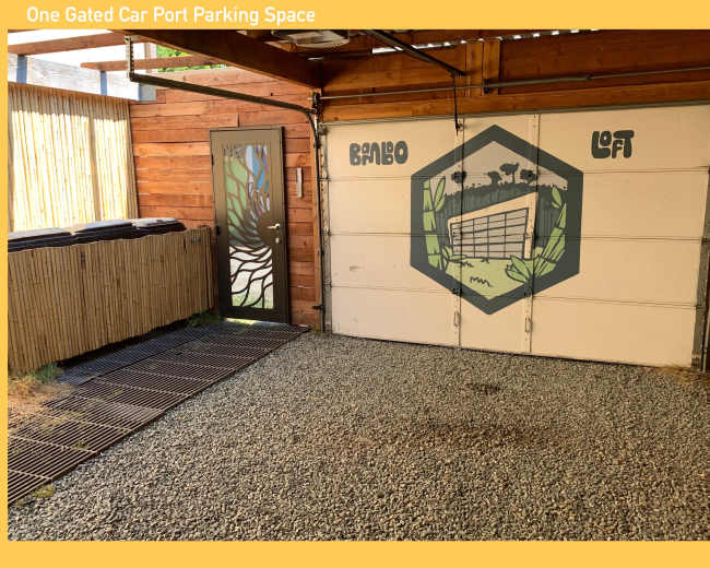 A gated carport parking space with a gravel floor, a decorated garage door featuring a design, and a door leading to an enclosed area with wooden slats.